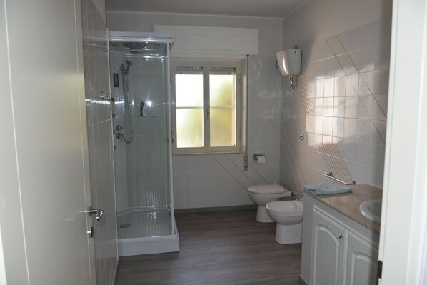 A bathroom with a glass shower enclosure, a toilet, and a sink with a towel rack.