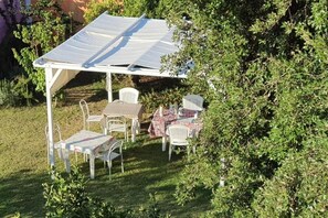 An outdoor patio with a white pergola, white metal chairs, and a table with a checkered tablecloth.