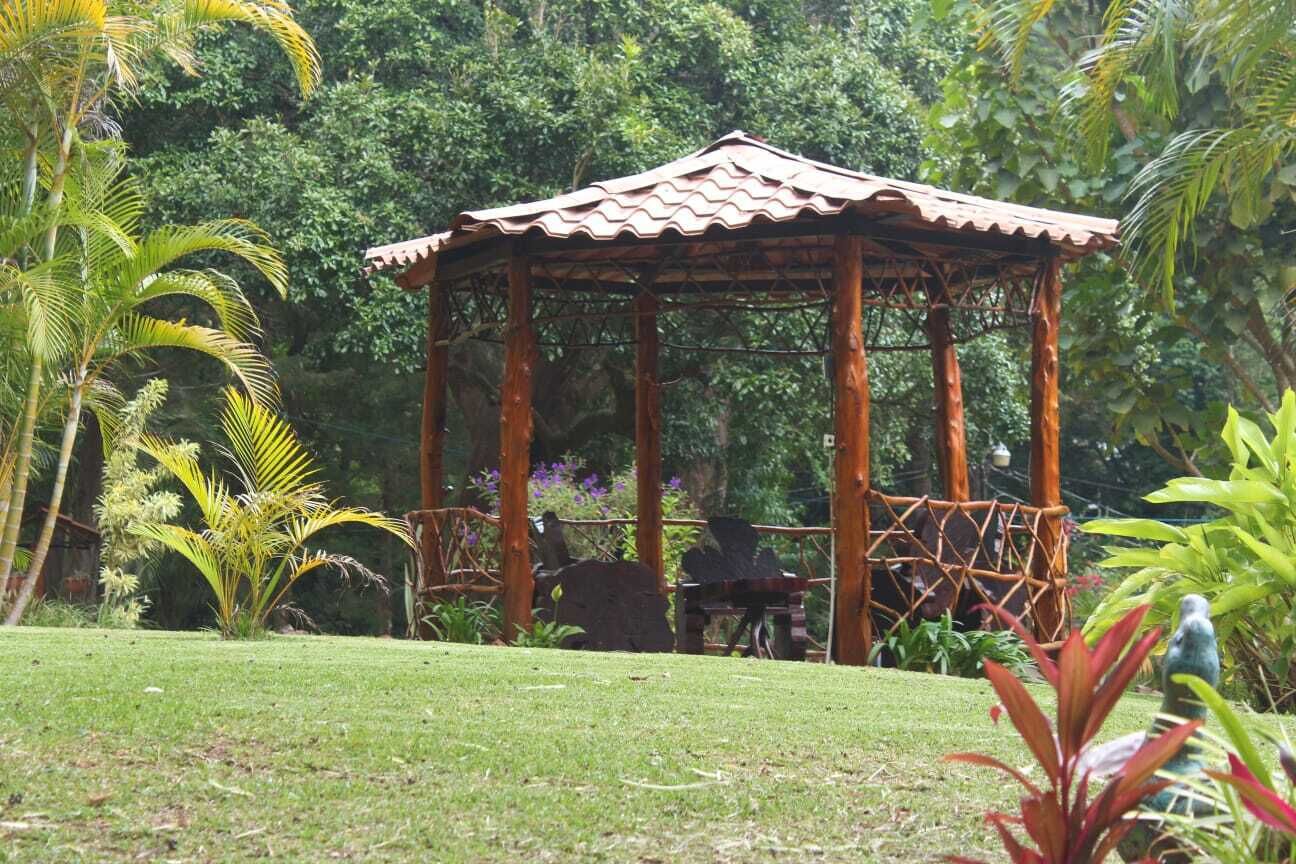 A gazebo with a tiled roof, surrounded by lush greenery and a well-maintained lawn.