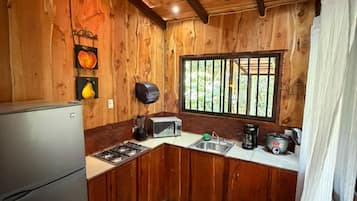 Cocina compacta con paredes de madera, un refrigerador, un microondas y un lavamanos.