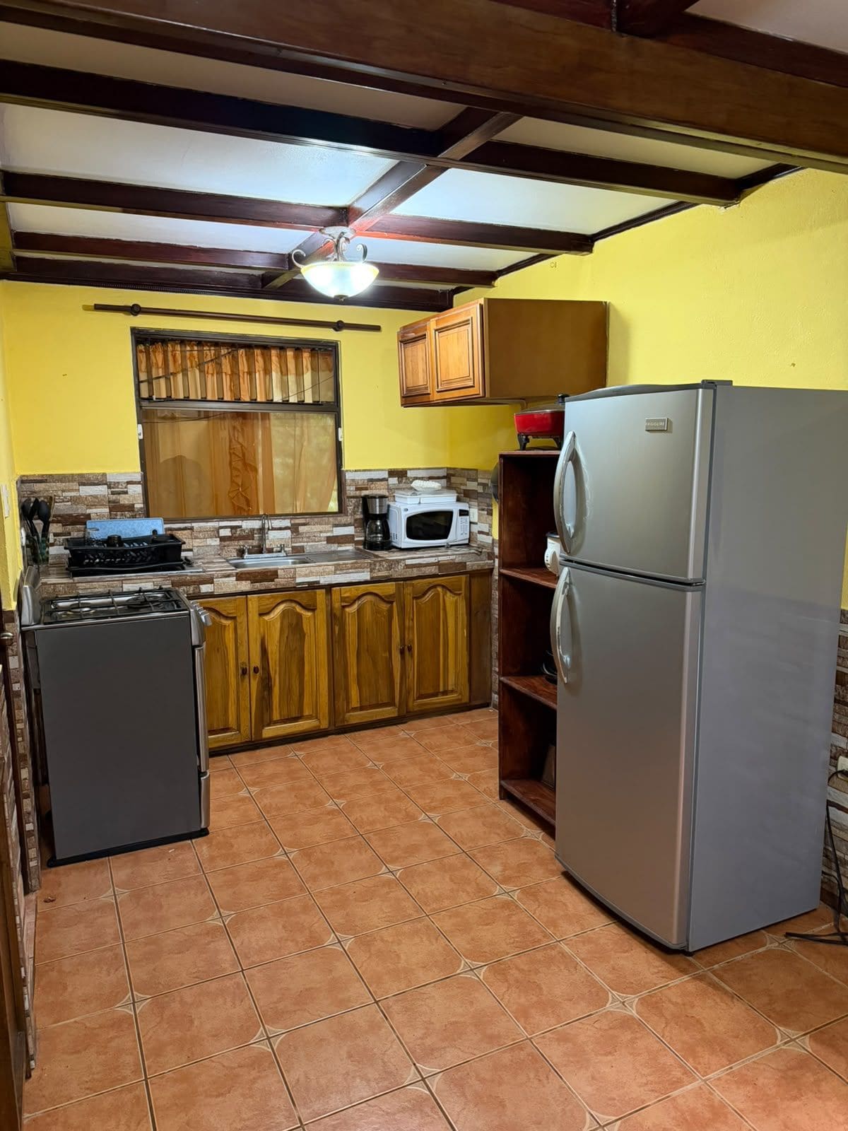 Una cucina compatta con mobili in legno, un frigorifero, un forno a microonde e un piano cottura a gas.