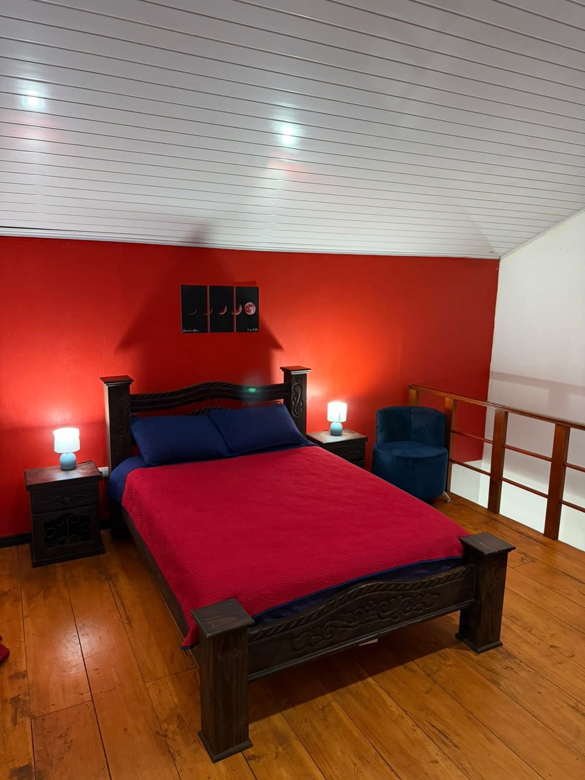 A bedroom with a wooden bed, red walls, and a nightstand with a lamp.