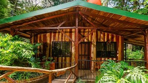 A rustic wooden structure with a green roof, surrounded by lush greenery and a small pond. - Cabañas Lunas del Poas  (Sabana Redonda)
