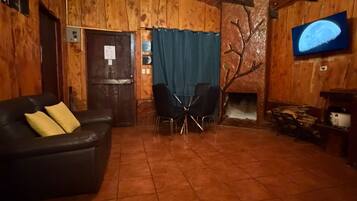 A wooden interior with a fireplace, a television mounted on the wall, a black leather sofa, and a tiled floor.