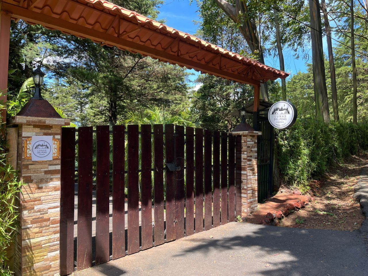 A gated entrance with a sign indicating 'Lunas del Poas' and a contact number.