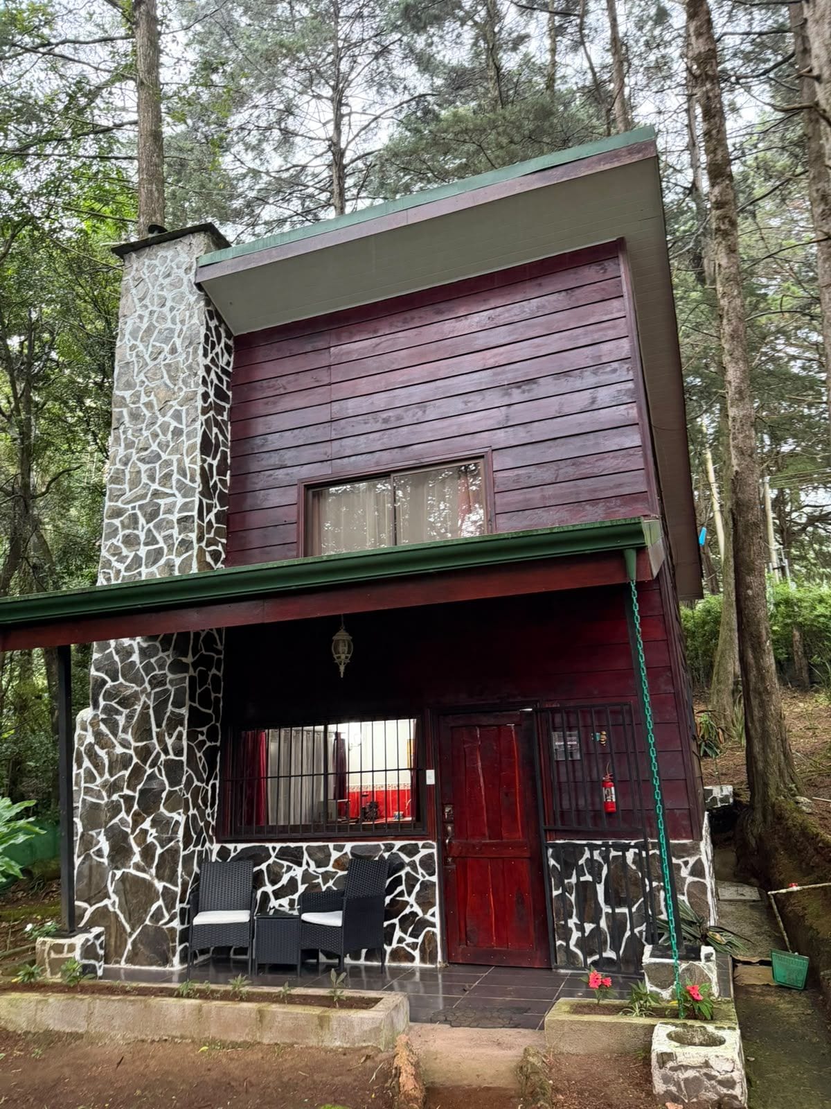 A two-story cabin with a stone facade, a red door, and a porch with outdoor seating.