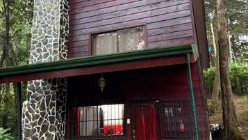 A two-story cabin with a stone facade, a red door, and a porch with outdoor seating.