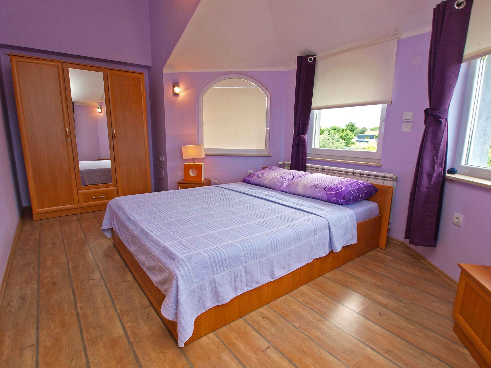 A bedroom with a bed, a wardrobe, a window with curtains, and a nightstand with a lamp.