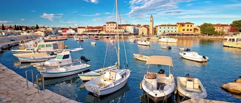 A marina with various boats docked, a stone quay, and buildings in the background.