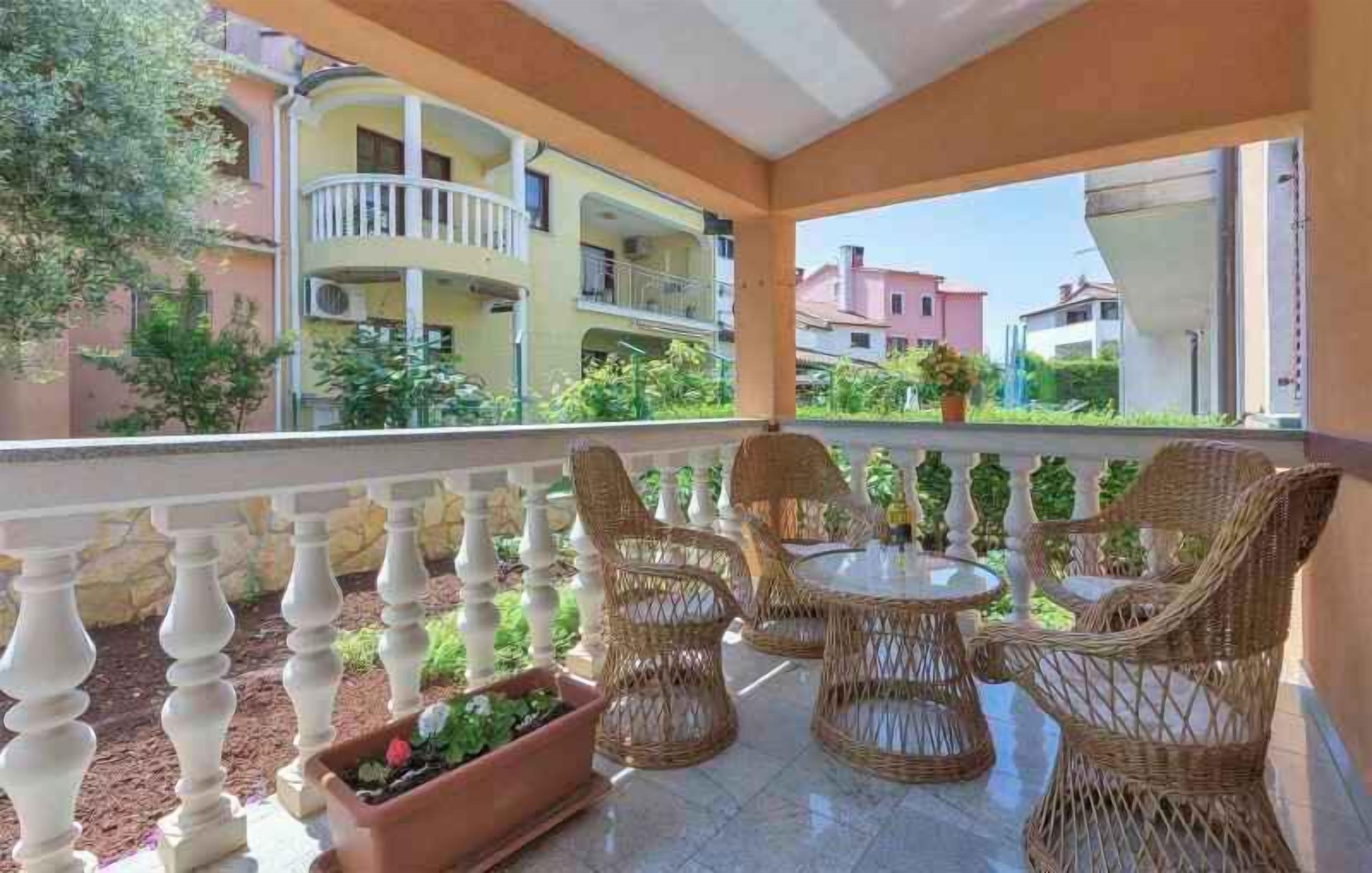 A balcony with wicker furniture, a view of multi-story buildings, and a clear sky.