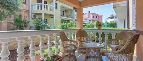 A balcony with wicker furniture, a view of multi-story buildings, and a clear sky.