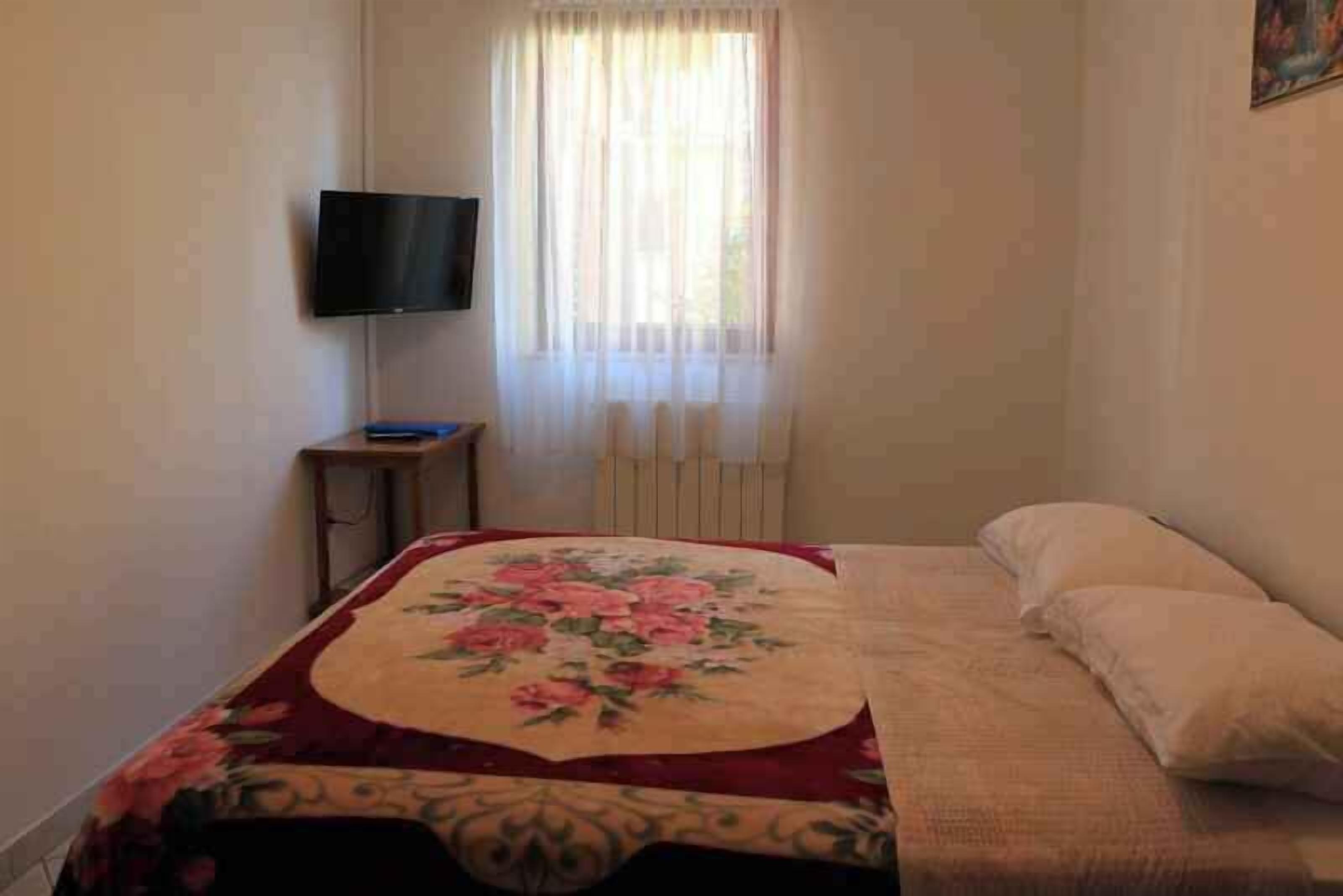 Una camera da letto con un letto, una televisione su un mobile, una finestra con tende e un termosifone.
