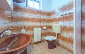 A bathroom with a ceramic sink, toilet, and tiled walls.