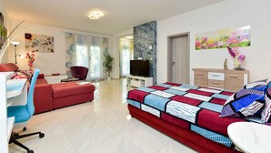 A modern bedroom with a bed, a desk, a red sofa, a TV, and artwork on the walls. - Holiday apartment with air conditioning (Valbandon)