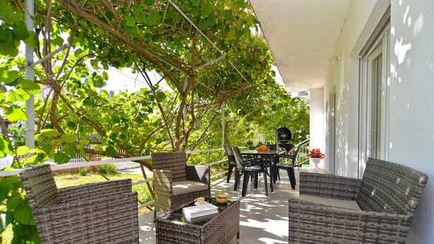 A covered outdoor seating area with wicker furniture and a table, surrounded by greenery. - Holiday apartment with air conditioning (Valbandon)