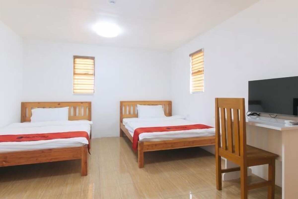 A room with two wooden beds, a desk with a chair, and a television.