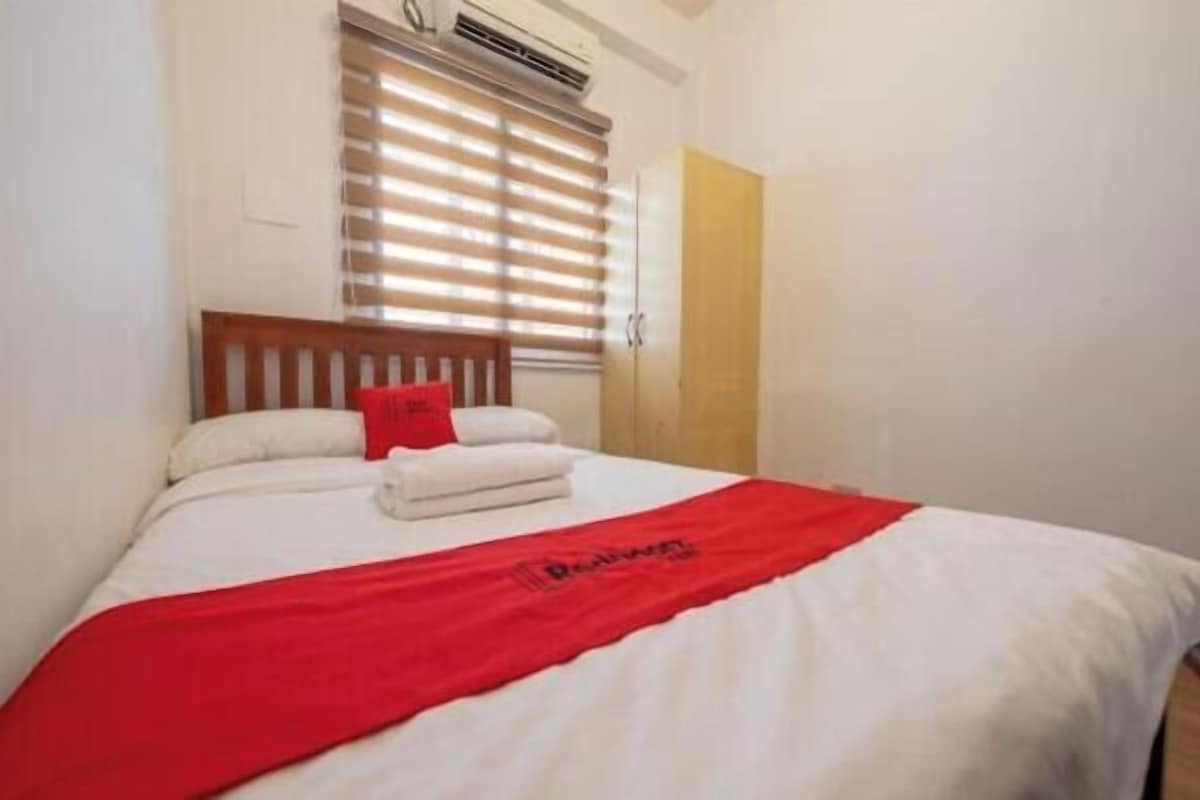 A single bed with a red blanket, white pillows, and a red pillow.