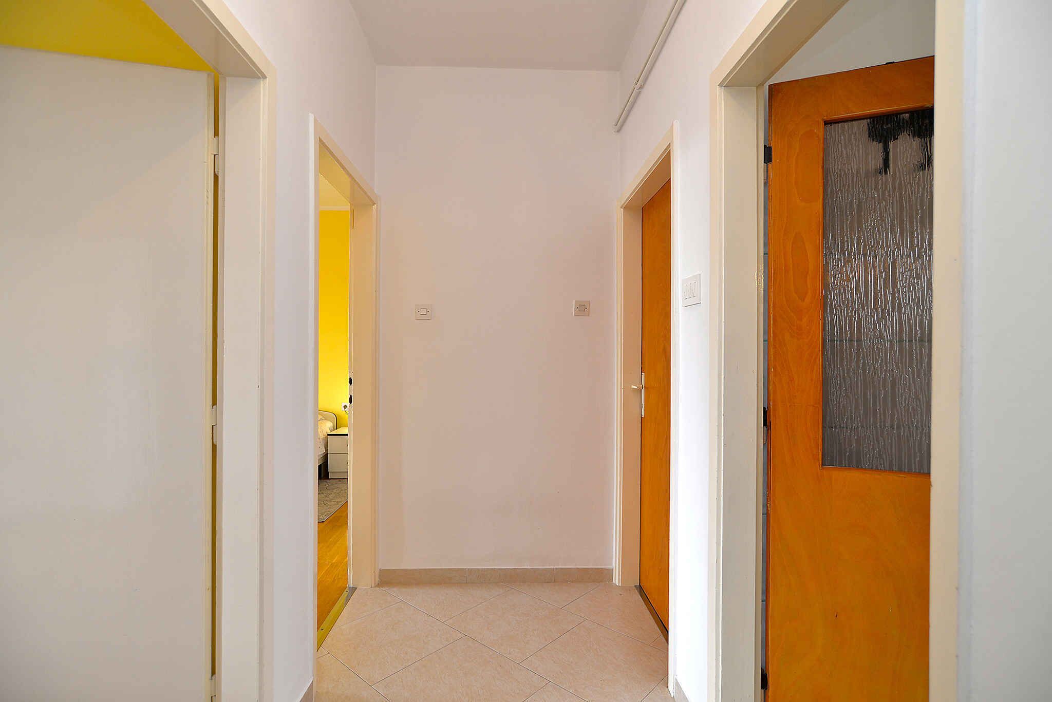 A narrow hallway with white walls and a yellow door on the left.