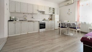 Une cuisine de taille réduite avec des meubles blancs, une cuisinière et un coin repas comprenant une table et des chaises.