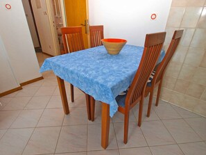 Un tavolo da pranzo con una tovaglia blu, circondato da sedie in legno, in una stanza con pavimento piastrellato e una porta sullo sfondo.