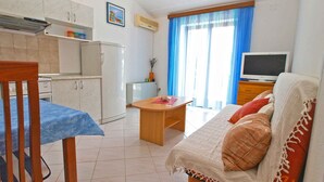 A compact living space with a kitchenette, a dining area, and a seating area with a sofa and a television. - Holiday apartment with balcony and air conditioning (Pula)