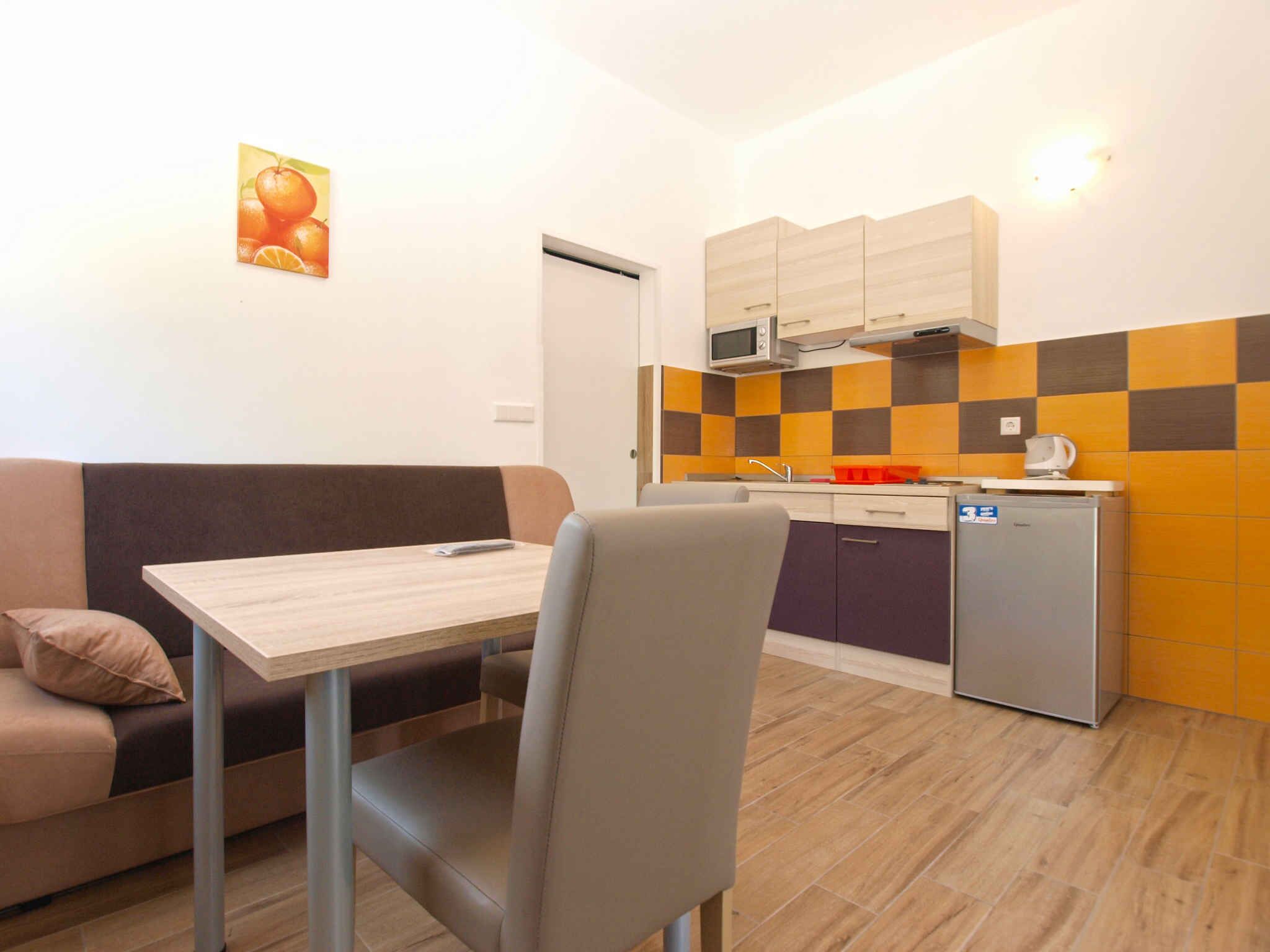 A compact kitchenette with a microwave, sink, and a small refrigerator. There is a dining area with a table and a chair, and a sofa with a cushion.