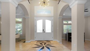 Ein geräumiges Foyer mit geometrischen Fliesen, doppelten Türen und einer dekorativen Deckenleuchte.