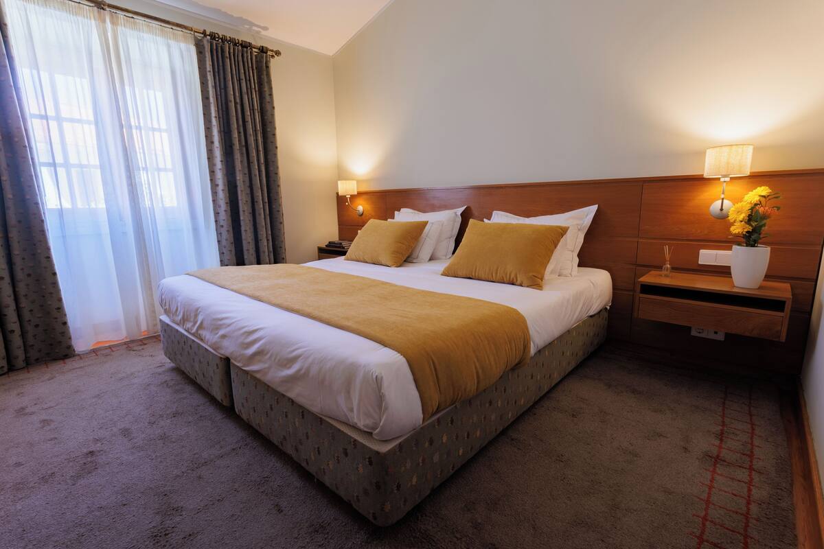 A hotel room with a large bed, two bedside tables, a nightstand, a lamp, and a vase with flowers.