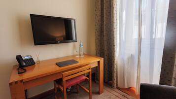 Habitación de hotel con escritorio de madera, televisor de pantalla plana, teléfono, ordenador portátil, botella de agua y una silla.