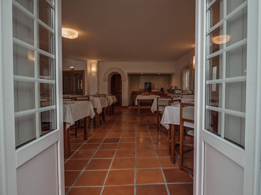 A dining area with tables and chairs, a kitchen in the background, and a tiled floor.