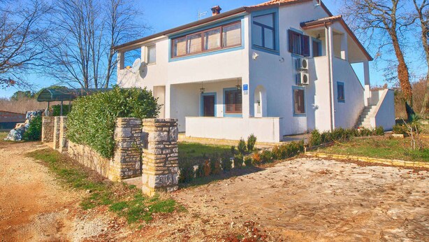 Una casa de dos pisos con una entrada de piedra, un porche cubierto y un cielo azul despejado.