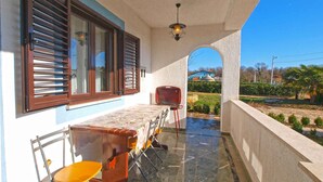 Un espacio al aire libre techado con una mesa y sillas, una silla roja, y una vista de una casa azul al fondo.