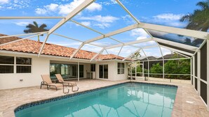 A swimming pool with a glass enclosure, surrounded by a patio area with lounge chairs.