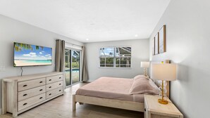 A bedroom with a bed, a TV, a dresser, and a window with blinds.