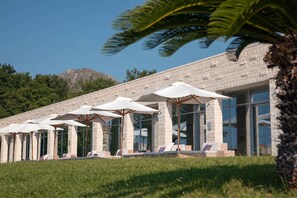 A modern building with a stone facade, outdoor seating with umbrellas, and a view of a mountain.