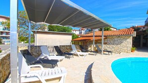 A poolside area with lounge chairs, a covered seating area, and a stone building in the background. - Holiday apartment with washing machine (Pula)