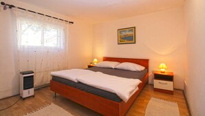 A bedroom with a wooden bed, two bedside tables with lamps, a heater, and a window with curtains. - Holiday apartment with washing machine (Pula)