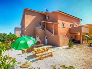 Un edificio de dos pisos con un patio, un horno de piedra y una sombrilla verde.