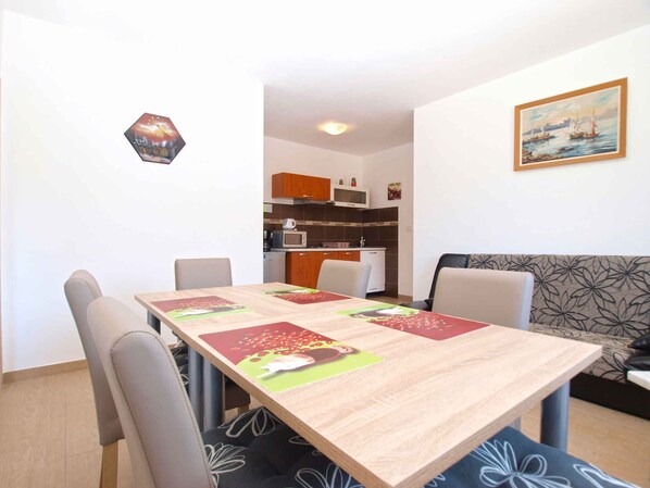 Un comedor con una mesa de madera y cuatro sillas, una cocina al fondo y un sofá con estampado floral.
