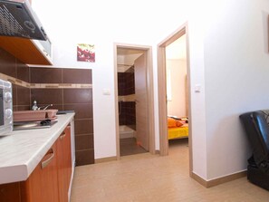 Cocina compacta con microondas, lavamanos y armarios, que da paso a un baño con ducha y una cama con ropa de cama naranja.