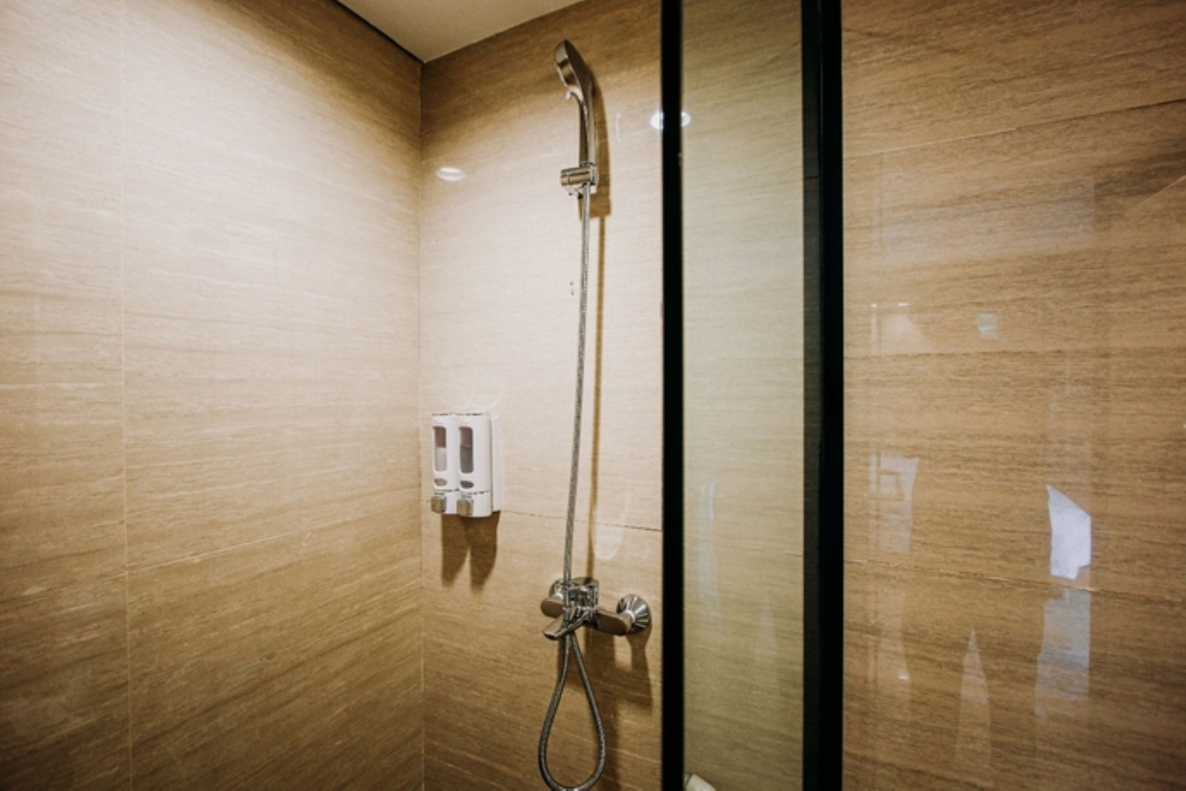 Un bagno moderno con box doccia in vetro, soffione a mano e dispenser di sapone a parete.