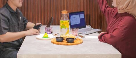 Two people at a table with a presentation screen behind them, a laptop, and a beverage on the table.