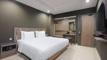 Una habitación de hotel moderna con una cama grande, una mesita de noche, un escritorio pequeño, un espejo y un televisor.