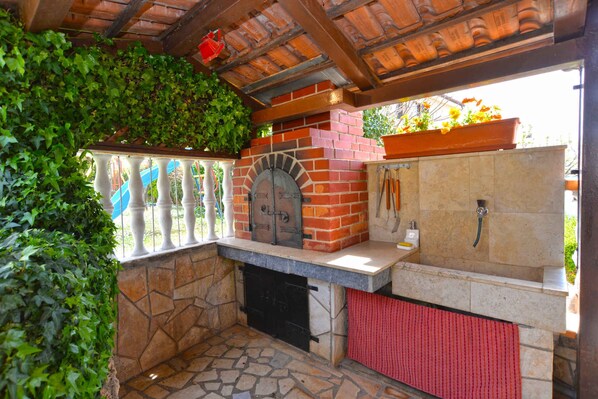An outdoor kitchen area with a brick oven, stone flooring, and a red towel hanging on the oven door.