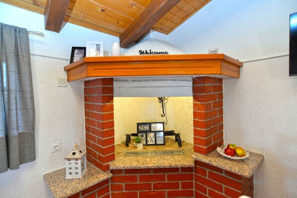 A brick fireplace with a 'Welcome' sign above it, a small shelf with a potted plant, and a fruit bowl on the right.