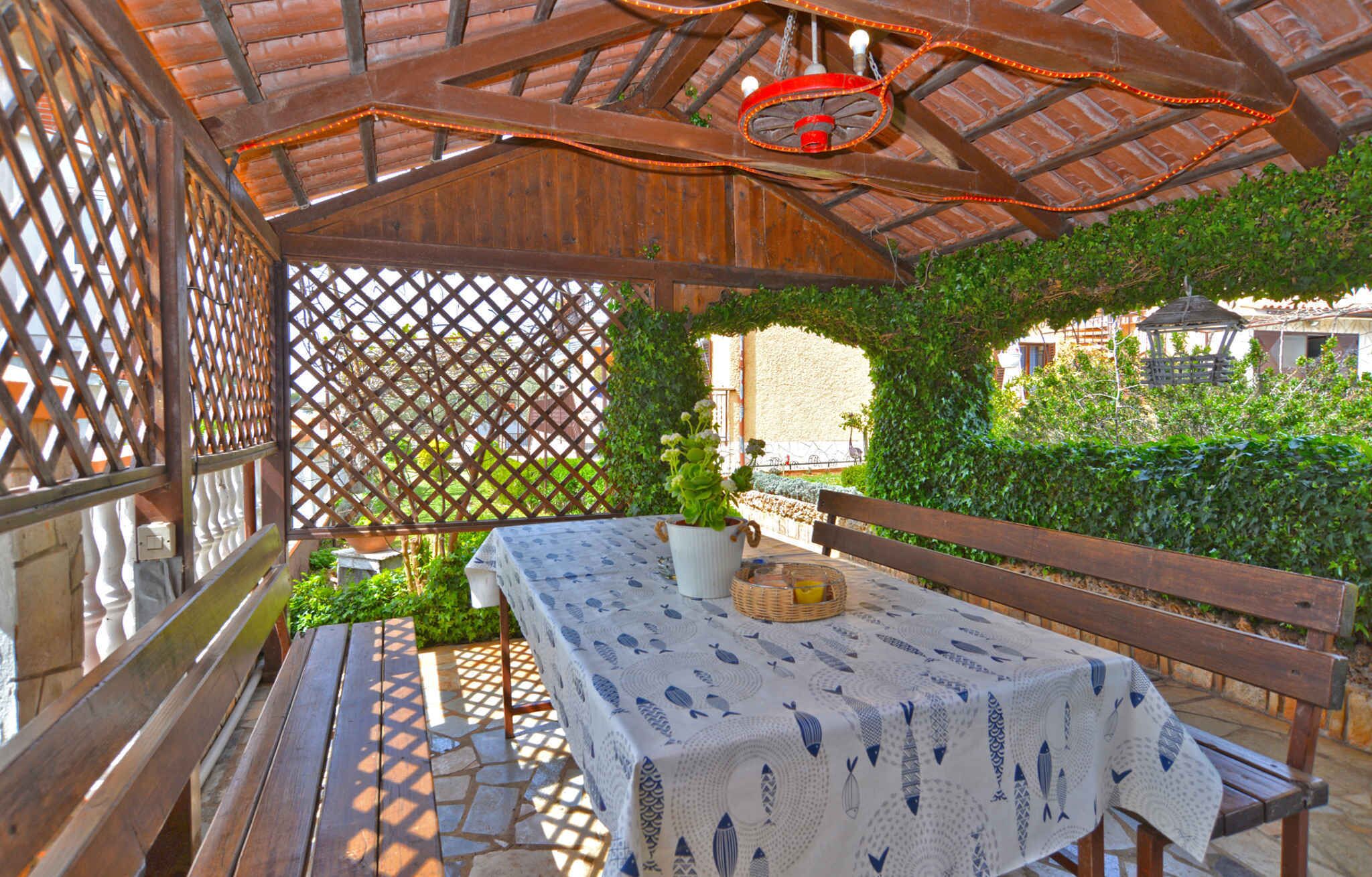 Un espace extérieur abrité, avec une table et des bancs, entouré de verdure et délimité par une clôture en treillis.