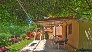A covered outdoor seating area with a stone patio, surrounded by lush greenery and flowering plants.