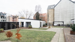 Une cour avec un petit bâtiment blanc, une grande grange blanche et une terrasse en bois.