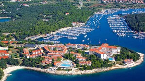 An aerial view of a coastal marina with numerous boats, a large hotel with red-roofed buildings, and a sandy beach area.