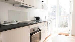 A modern kitchen with white cabinets, a black countertop, and an oven. There is a window with a view of buildings outside. - Beautiful 2-bed w Large Balcony (Copenhagen)